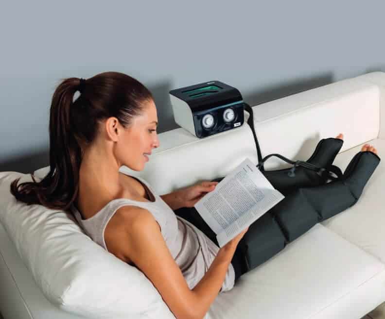 Patiente utilisant l'appareil de pressothérapie I-Press LEG2 I-Tech avec 2 bottes sur un canapé